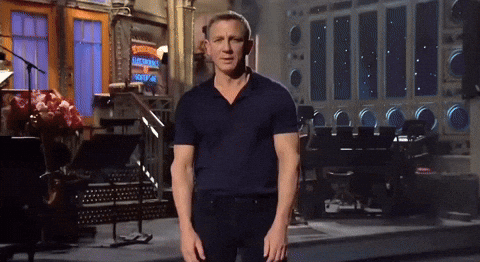 Animated clip of a man in a dark polo shirt standing on a television studio stage.